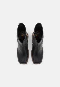 Bottines en cuir noir avec un bout carré, fermeture éclair latérale et semelle beige. Texture lisse avec un design minimaliste et des garnitures dorées.