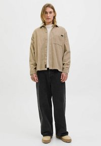 Tan corduroy shirt met een voorzak, gecombineerd met zwarte wijde jeans en beige schoenen. Eenvoudig knoopontwerp met opvallende textuur.