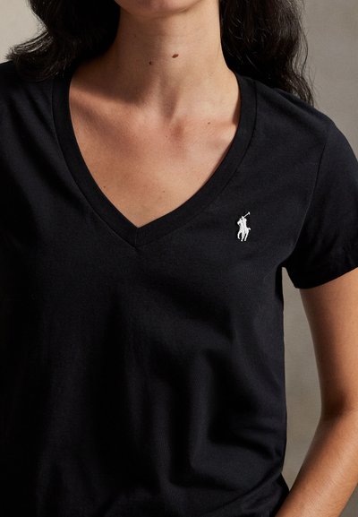 Γυναίκα που φοράει μαύρο T-shirt με V-λαιμόκοψη και μικρό λευκό λογότυπο παίκτη πόλο στην αριστερή πλευρά του στήθους.