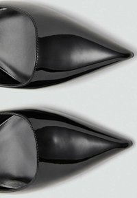 Mules en cuir verni noir avec un bout pointu et une texture lisse. Présentent un design à enfiler et des coutures minimales le long du bord.