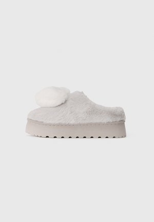 Pantufa cinza peluda com detalhe de pompom branco redondo, sola plana com ranhuras, textura suave e design de abertura na parte de trás.
