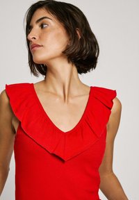 Top rosso senza maniche con scollatura a V profonda e ampie ruches lungo il collo; texture liscia e a coste con design aderente.