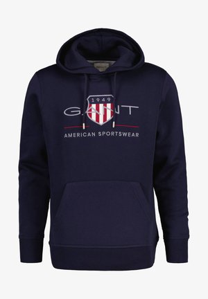 Tumesinine kapuutskait vest, mis on valmistatud puuvillast. Omab esiosas asuvat kangaroo taskut, soonikvarrukaid, reguleeritavat kapuutsit ning grafitööstuslikku logo punaste ja valgete elementidega.