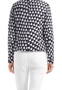 Chaqueta con patrón geométrico en blanco y negro, con un diseño ajustado, mangas largas y dobladillo recto, combinada con jeans blancos.