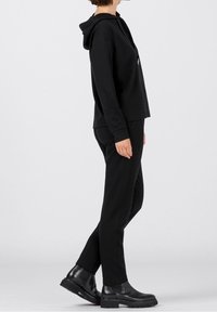 Černá mikina s kapucí a odpovídající kalhoty, obojí z měkké, strukturované tkaniny. Doplněno robustními černými kotníkovými botami. Jednoduchý, moderní design.