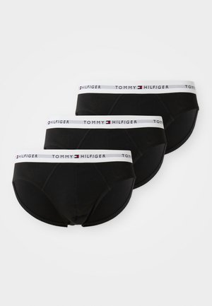 Tre slip da uomo neri con fascia elastica bianca in vita, caratterizzati dal logo Tommy Hilfiger e motivo a bandiera, disposti in fila sovrapposta.