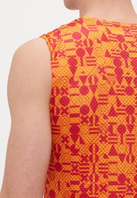 Ujjatlan felső, élénk narancssárga és piros geometrikus mintával, amely köröket, háromszögket és csíkokat tartalmaz. Az anyag könnyűnek és texturáltnak tűnik.