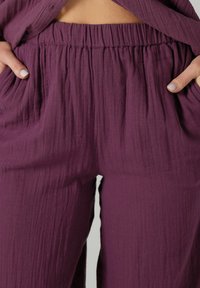 Pantalons légers violets en tissu texturé, dotés d'une taille élastique et de poches latérales. Le matériau semble doux et fluide.