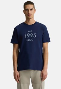 T-shirt in cotone blu navy con scollatura a girocollo e grafica frontale con la scritta: "est. 1995 LIUJO" in grigio chiaro. Maniche corte e vestibilità rilassata.
