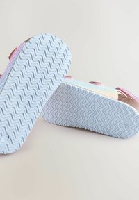 Rosa und schimmernde Sandalen mit verstellbaren Riemen, strukturierten weißen Gummisohlen mit einem wellenförmigen Muster, von unten betrachtet.