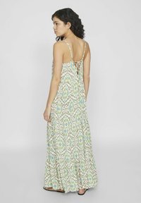Vestido maxi con tirantes ajustables, estampado en verde y azul sobre un fondo crema, presenta una silueta fluida y una espalda baja con detalles de encaje.