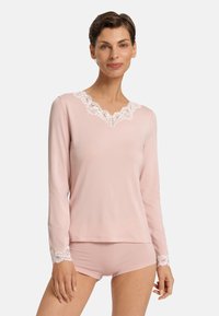 Top de manga larga rosa claro con escote de encaje y detalles de encaje en las mangas, combinado con unos pantalones cortos a juego con acentos de encaje. Textura de tela suave.