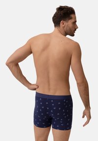 Námořnické modré trenýrky s geometrickým vzorem v světle modré barvě. Elastický pas a přiléhavý střih. Materiál vypadá měkce a pružně.