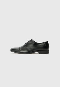 Chaussure habillée en cuir noir avec un bout pointu, des lacets et des détails de couture subtils. Dotée d'un petit talon carré et d'une finition lisse et brillante.