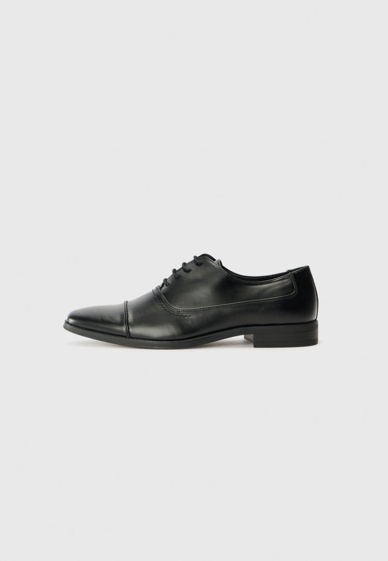 Black leather dress shoe with a pointed toe, laces, and subtle stitching details. Features a low block heel and smooth glossy finish.