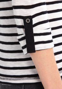 Czarna i biała koszula w paski z półrękawami. Mankiet ma czarny akcent i srebrny detal w postaci guzika. Miękka, dzianinowa struktura.