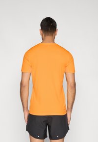 Sportliches T-Shirt mit kurzen Ärmeln aus leuchtend orangefarbenem Stoff, glatter Textur, figurbetontem Schnitt, mit rundem Ausschnitt und ohne sichtbare Markenzeichen.