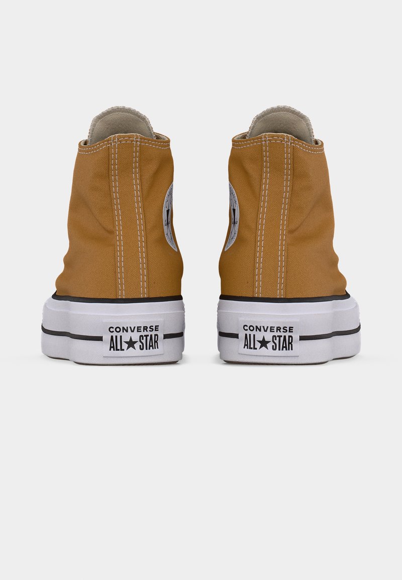 Sneakers Converse All Star alte in tela color senape con suole in gomma bianca e dettagli neri, caratterizzate da un logo circolare sul lato.