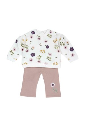 Top bianco a maniche lunghe con stampa floreale multicolore abbinato a pantaloni malva con un singolo fiore sulla gamba sinistra.