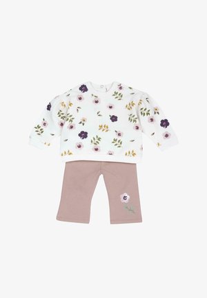 Hvid langærmet top med flerfarvet blomstermønster kombineret med lilla bukser med en enkelt blomst på venstre ben.