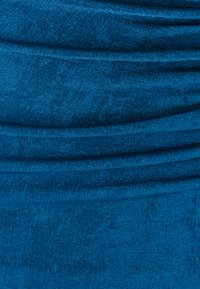 Tyrkisblåt stof med en struktureret overflade, der har opsamlede og draperede sektioner. Glansen fremhæver dets bløde, glatte finish.