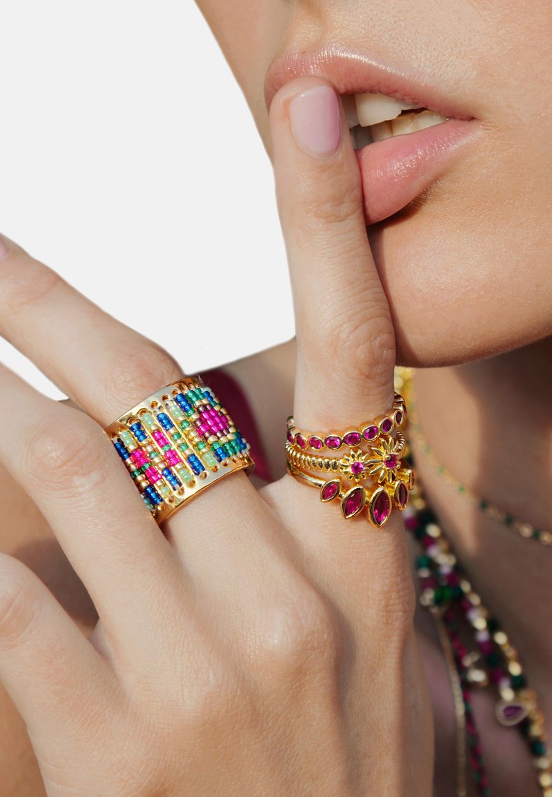 Bague en ton doré avec des motifs complexes : une large bande ornée de perles colorées et deux bandes plus fines décorées de pierres roses et d'accents floraux.