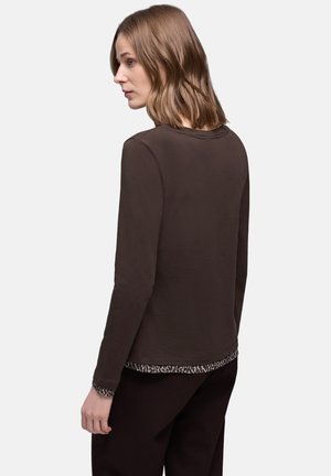 Ruskea pitkähiha paita pyöreällä pääntiellä, jossa on teksturoitu, kuvioitu helma ja sileä kangas. Yksinkertainen, rento muotoilu.