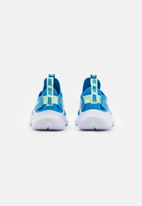 Een paar blauwe en witte Nike sneakers van achteraf weergegeven, met groene Nike-merk trekbanden op de hiel en witte gestructureerde zolen op een witte achtergrond.