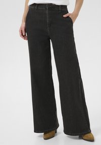 Črne široke kavbojke z visokim pasom, narejene iz denima, z sprednjimi žepi in zadrgo. Tkanina ima rahlo teksturo.