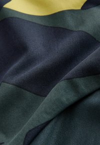 Textil mit überlappenden geometrischen Formen in Dunkelgrün, Marineblau und Gelb. Glatte, gewebte Textur mit leichtem Glanz.