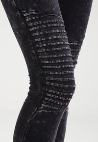 Černé denimové legíny s děrovanými panely na kolenou a omytou texturou, zdůrazňující přiléhavý design.
