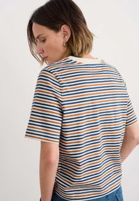 Camiseta de manga corta a rayas en color crema, con rayas horizontales azules, naranjas y marino. Cuello acanalado, tejido de algodón suave, corte relajado.