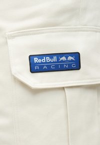 Μπλε λογότυπο Red Bull Racing ραμμένο σε τσέπη από κρεμ ύφασμα, που δείχνει δύο ταύρους να κοιτούν ο ένας τον άλλον πάνω από το όνομα της μάρκας.