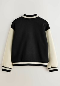 Sudadera negra y crema con un diseño corto, cuello y puños acanalados, y un bloqueo de color en las mangas en contraste. Tejido suave y texturizado.