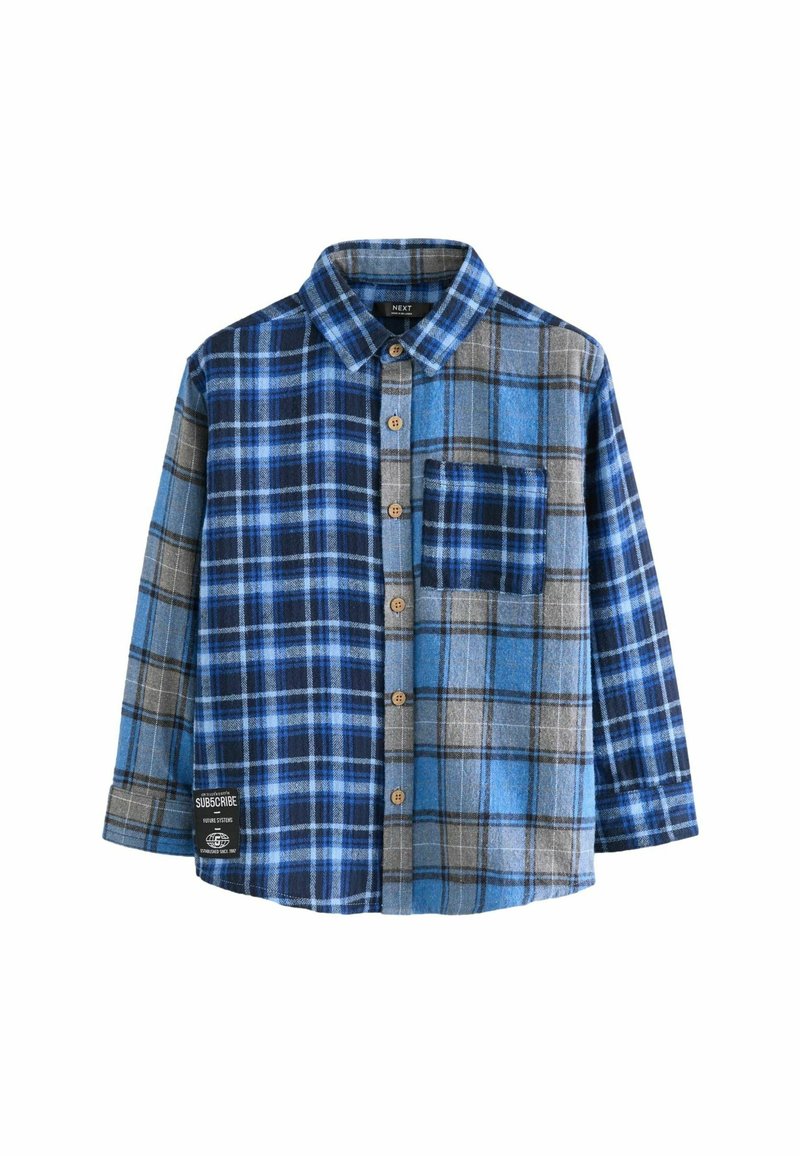 Chemise à manches longues à carreaux bleu et gris avec poche frontale, boutons en bois et un écusson noir et blanc près de l'ourlet.