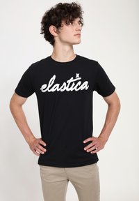 Černé bavlněné tričko s bílým textem "elastica" v tučném, hravém písmu; krátké rukávy, kulatý výstřih, uvolněný střih.