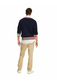 Maglione navy a trama a trecce con dettagli a righe rosse e bianche, indossato sopra una camicia bianca e abbinato a pantaloni beige e sneakers bianche.