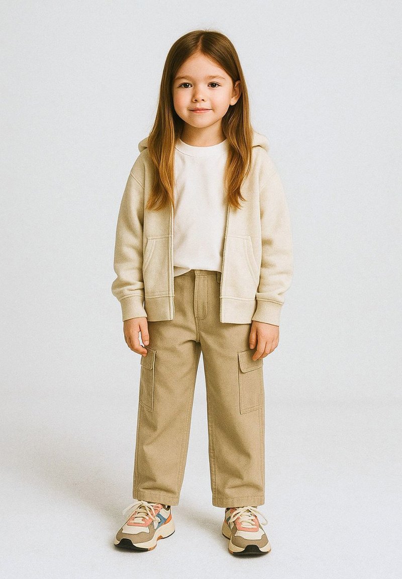 Sudadera beige con cremallera, camiseta blanca, pantalones cargo color caqui con grandes bolsillos y zapatillas de colores con suelas texturizadas. Conjunto casual infantil.