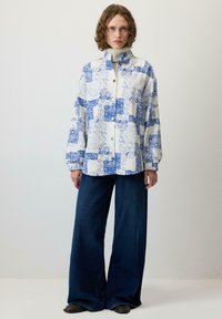 Jachetă cu nasturi, cu un model albastru și alb, cu mâneci lungi și guler înalt, asortată cu blugi din denim închis la culoare, cu croială largă.