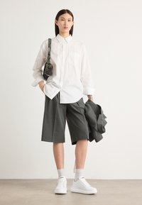 White button-up shirt, gray pleated shorts, white sneakers, and a small black bag. The fabric appears smooth and structured with a casual fit.