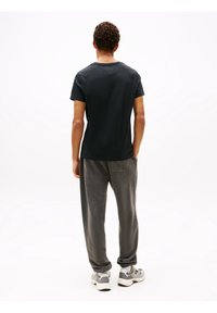 Men's black cotton t-shirt with short sleeves, relaxed fit. Paired with gray sweatpants and gray athletic shoes, captured from the back.