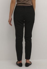 Svarta mönstrade byxor med rutig design, med en åtsittande passform och elastisk midja. Bärs med platta svarta skor.