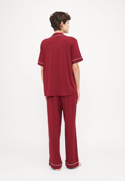 Burgundy pajama set featuring a short-sleeve shirt and long pants with white piping accents. Soft, lightweight fabric, relaxed fit.