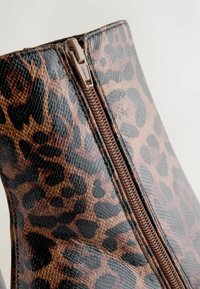 Leopard print ankle boot made of glossy textured material with a side zipper and contrasting brown accents.