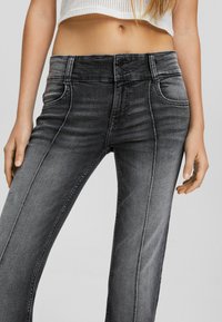 Los jeans de mezclilla gris presentan una cintura alta, dos botones, bolsillos delanteros y un corte recto con un ligero desvanecimiento en la superficie.