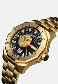 Goudkleurig achthoekig horloge met een zwarte wijzerplaat, witte uurmarkeringen, oranje accenten en een gestructureerde metalen band. Bevat een datumaanduiding.