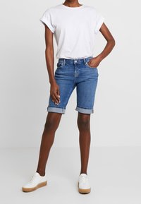 Lichtblauwe denim shorts met omgeslagen zomen, gecombineerd met een wit T-shirt met korte mouwen. Witte sneakers met een beige plateauzool.