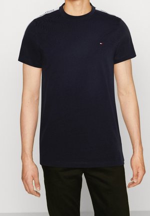 Marineblaues Baumwoll-T-Shirt mit Rundhalsausschnitt, kurzen Ärmeln und weißen Akzentstreifen auf den Schultern. Verfügt über ein kleines Logo auf der Brust.