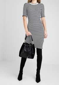 Musta-valkoraidallinen ribbineulottu mekko aaltoilevilla hihoilla, yhdistettynä mustaan kantolaukkuun, jossa on logo ja nyörikiristys.