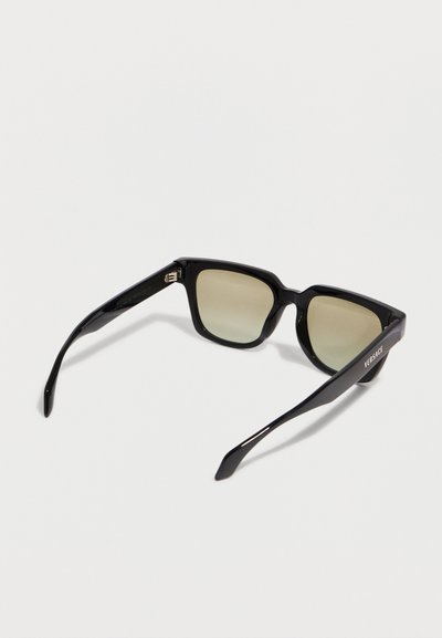 Γυαλιά ηλίου με μαύρο τετράγωνο πλαίσιο, φακούς με σκουρόχρωμη απόχρωση και το λογότυπο "Versace" στον δεξιό βραχίονα, εμφανιζόμενα σε λευκό φόντο.